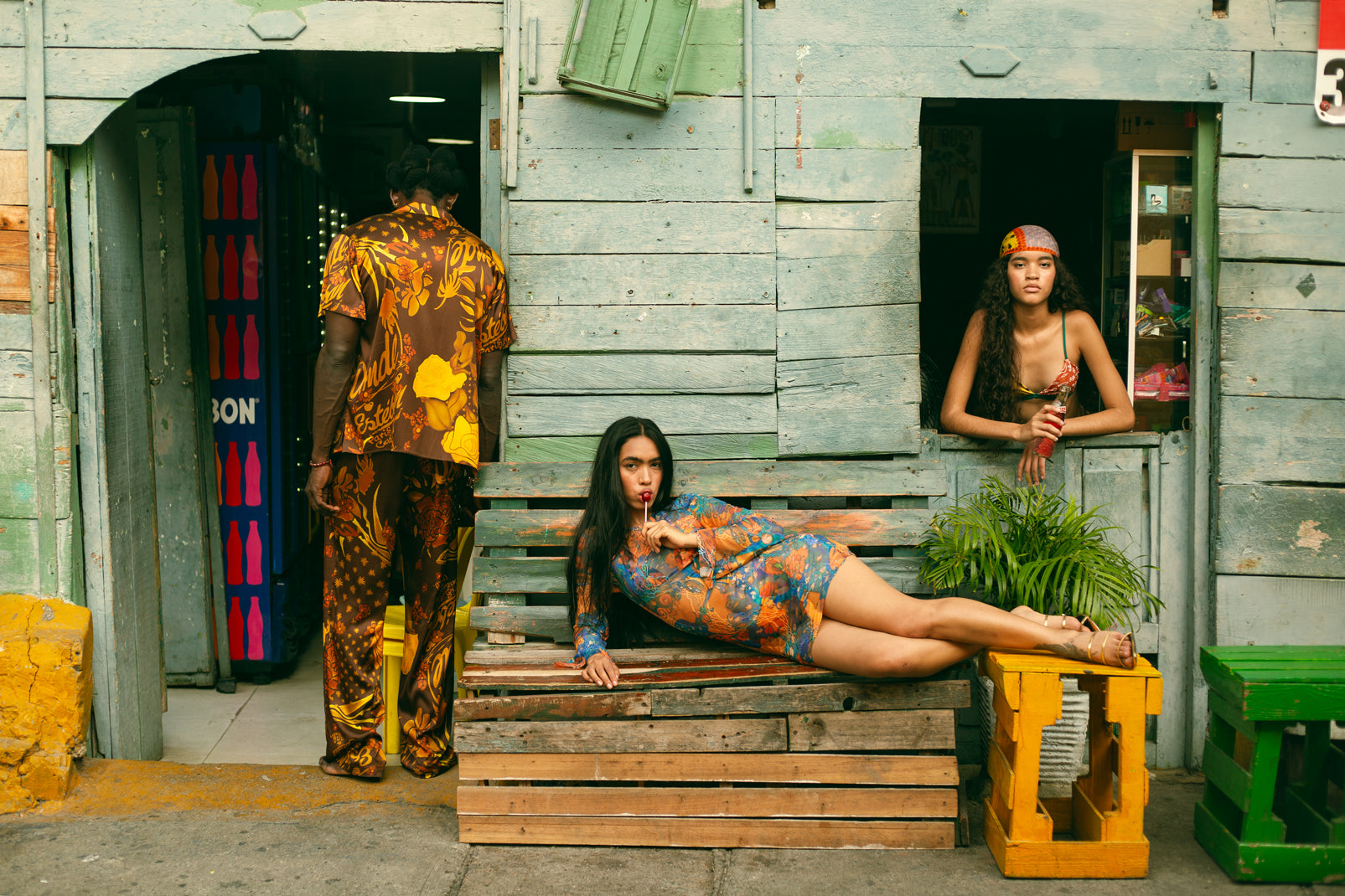 Three people in colorful outfits in front of a rustic wooden building.